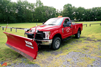 Ford F-350 Super Duty truck with a front plow in a field, red body, single rear wheel, utility branding on door.