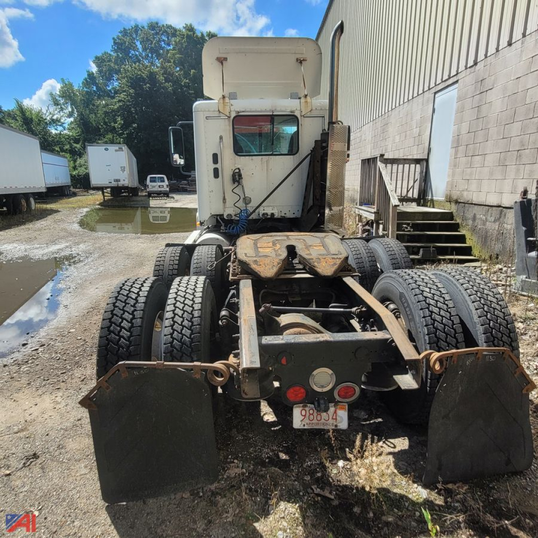 Truck chassis rear view showing dual rear axles and mounting brackets; visible license plate with 9 8 8 3 4; mud flaps; Freightliner Columbia 120 cab in background.