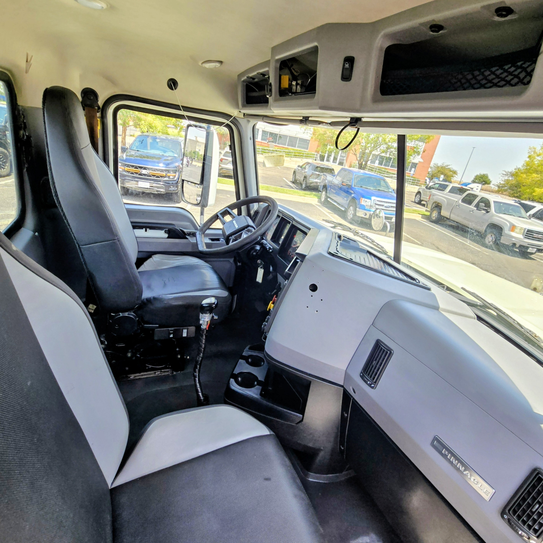 Truck cab interior of a 2020 Mack PI64T showing driver seat, steering wheel, dashboard, and passenger seat with a view through the windshield.