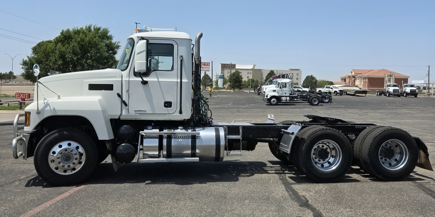 Truck chassis side view showing cab and six-wheeled rear axle configuration with fuel tanks and steps, white cab, black chassis, clear daytime sky.