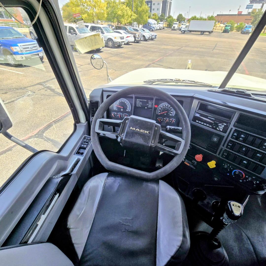 Interior of a 2020 Mack PI64T cab displaying steering wheel with Mack logo, dashboard gauges, and control panel; view through the driver’s door and windshield.