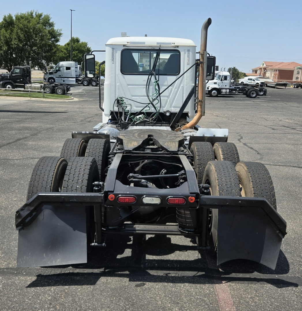 Rear view of a Mack PI64T conventional daycab truck showing dual rear axles, chassis, exhaust stack, and mud flaps.