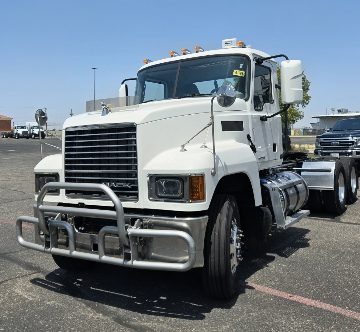 Truck front view of a 2020 Mack PI64T conventional daycab showing large chrome grille, bumper guard, dual exhaust, and front wheels.