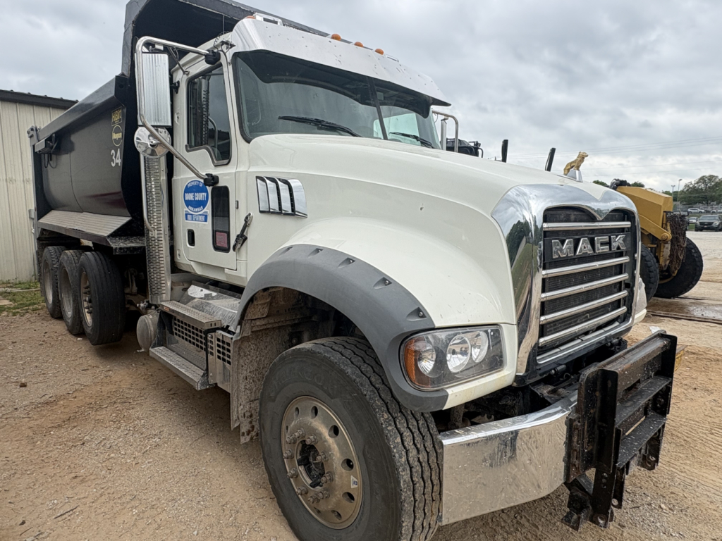 Mack GR84F dump truck with white cab and chrome grille, front bumper guard, dual rear wheels, and dump bed visible; VIN tag and stock number not readable.