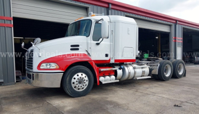 Mack Pinnacle cab and chassis truck, side view, white cab with red lower body stripe, multiple rear axles, fueling tanks visible, in a service lot.