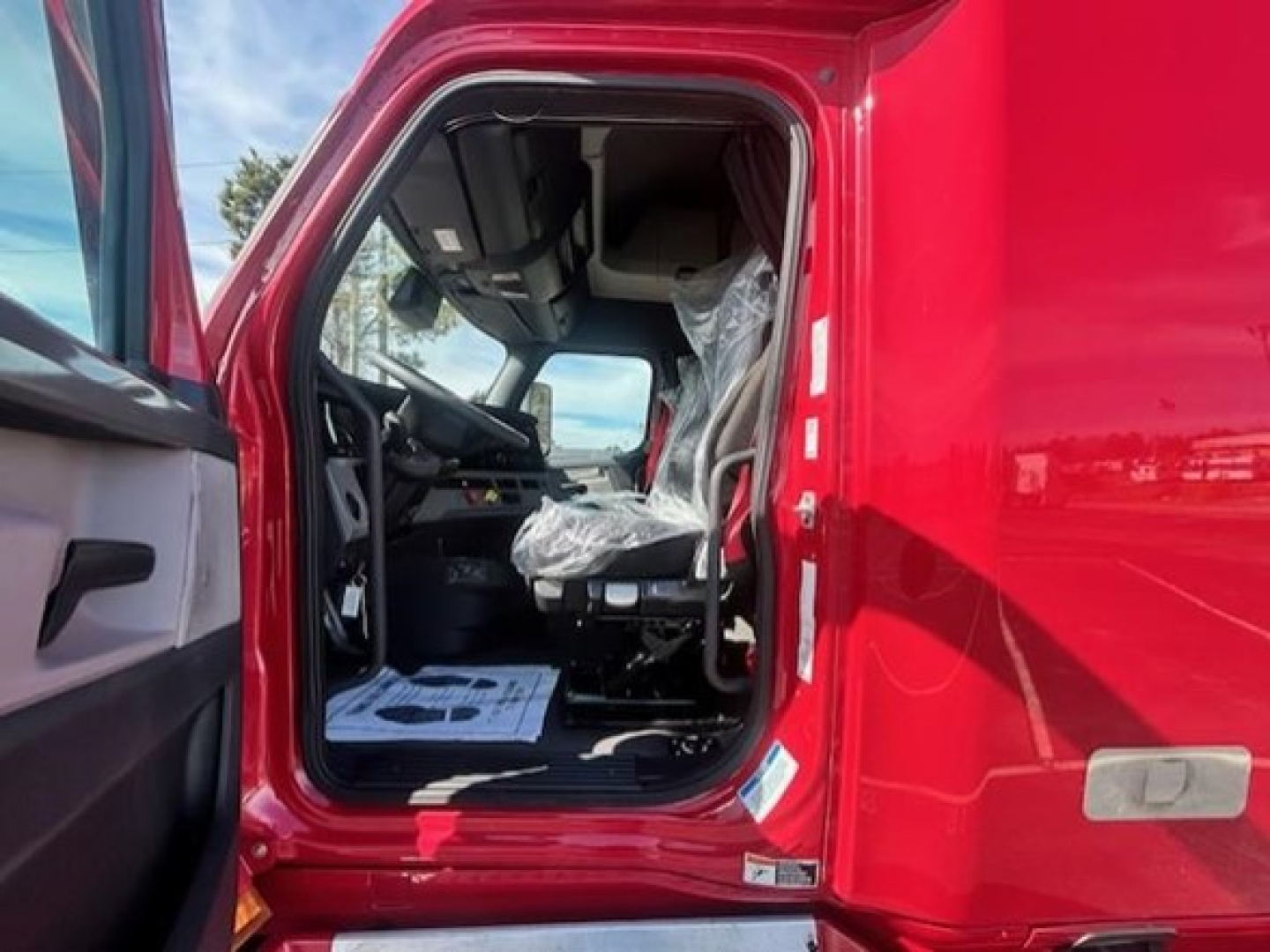 Truck cab interior of a red 2022 Freightliner Cascadia 126, front door open showing driver seat and dashboard.