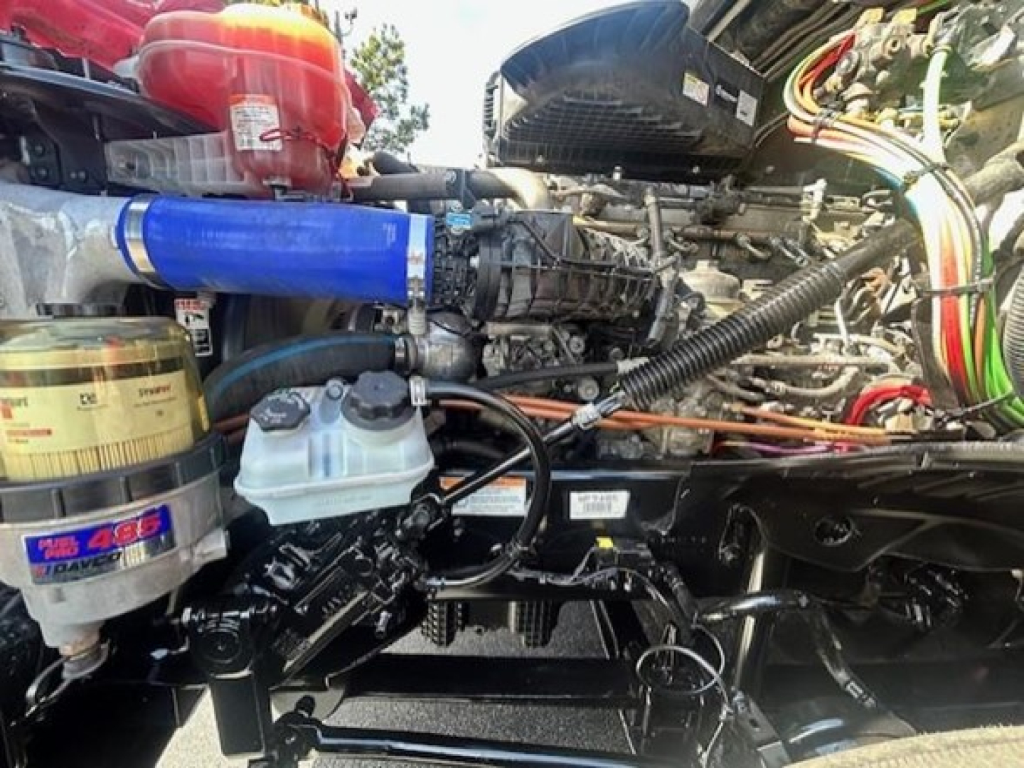 Freightliner Cascadia 126 engine bay showing coolant reservoir, blue intercooler hose, and various wiring in view.