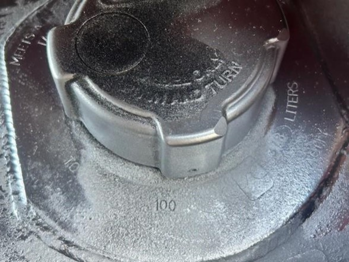 Fuel tank cap with surrounding markings showing 100 liters capacity and metallic surface.