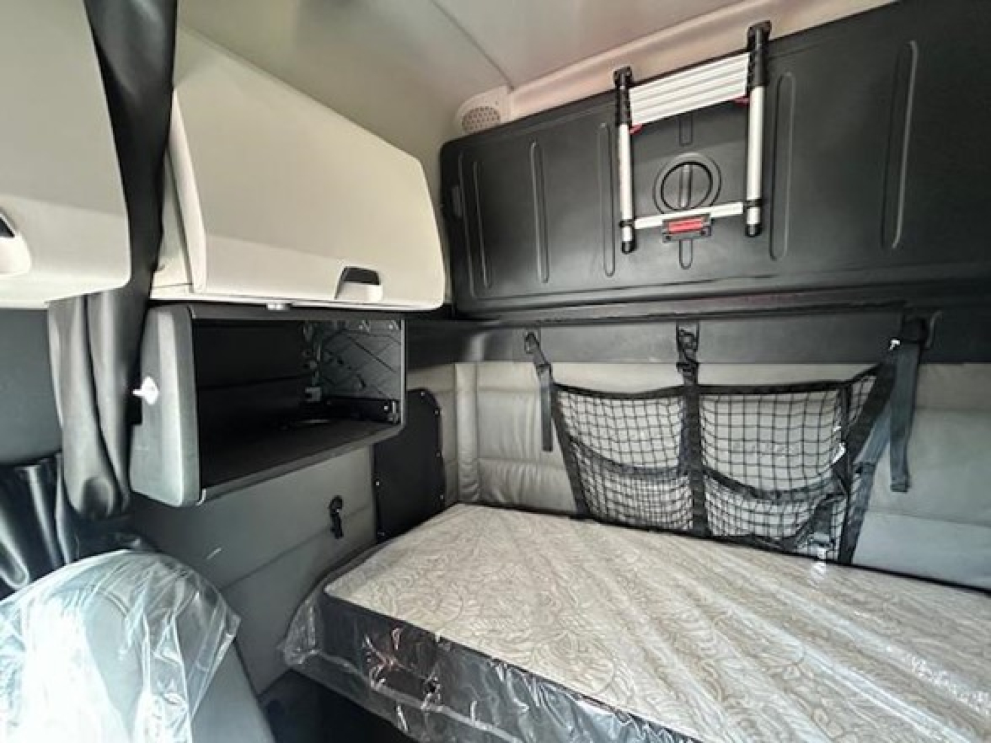 Cabin interior of a 2022 Freightliner Cascadia 126 sleeper showing bunk bed area with storage shelves and net storage on wall.