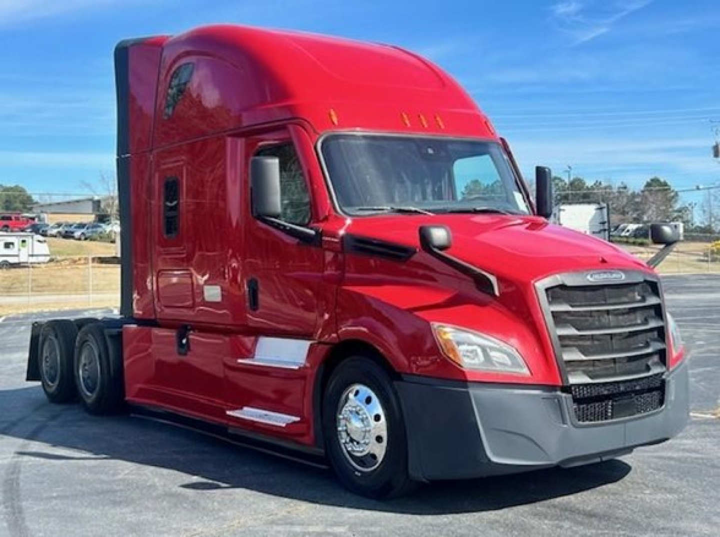 Red Freightliner Cascadia 126 tandem tractor cab with sleeper in a dealership lot; visible text includes windshield and side window reflections but no legible labels.