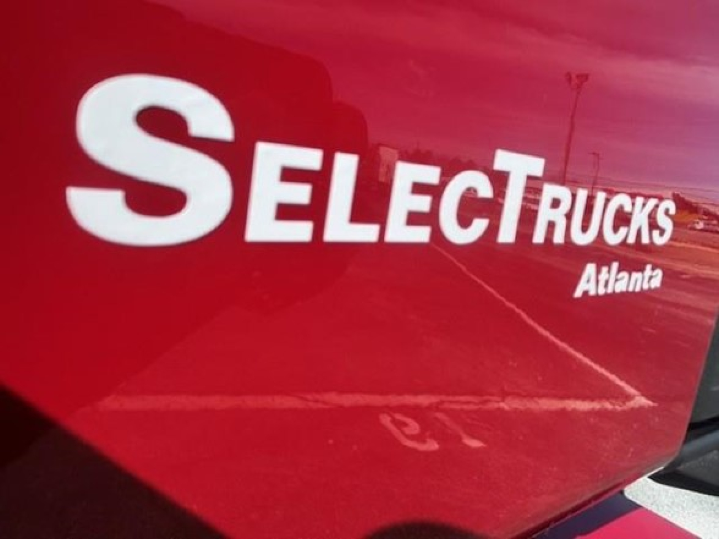 Truck cab with SelectTrucks Atlanta logo on red surface, partial photo of exterior panel.