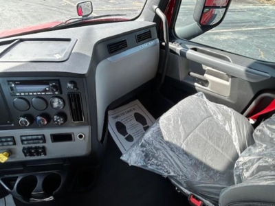 Cab interior of a Freightliner Cascadia 126 truck showing dashboard with control panel, steering column area, and passenger seat covered in plastic.