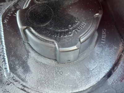 Fuel tank cap with surrounding markings showing 100 liters capacity and metallic surface.