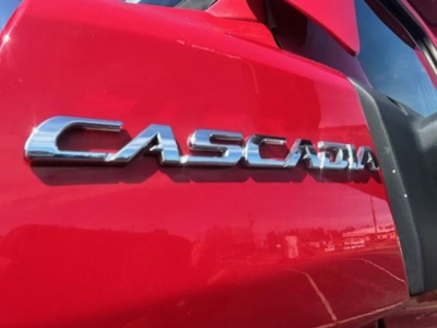 Close-up of red Freightliner Cascadia badge on cab door showing chrome 'CASCADIA' lettering.