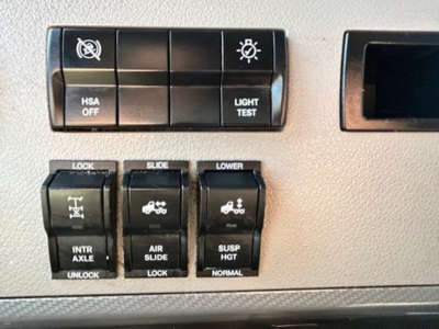 Truck dashboard panel with switches labeled HSA OFF, LIGHT TEST, LOCK, SLIDE, LOWER, INTR AXLE UNLOCK, AIR SLIDE LOCK, SUSP HOT NORMAL, showing control buttons.