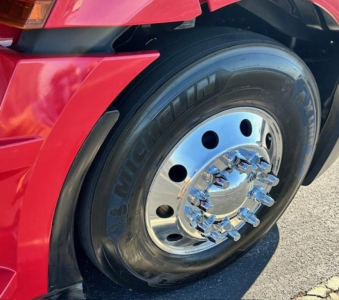 Freightliner Cascadia front wheel and tire showing chrome hub with lug nuts and red fender.