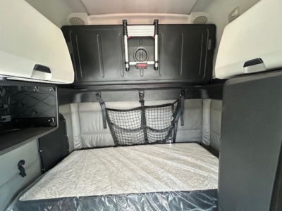 Freightliner Cascadia interior sleeper area showing bunk storage under cabinet and netted pocket, light gray upholstery and overhead panels.