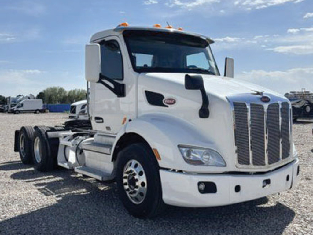 Peterbilt 579 conventional daycab truck side/front view, white, with tall grille and dual rear axles, stock number 552640.