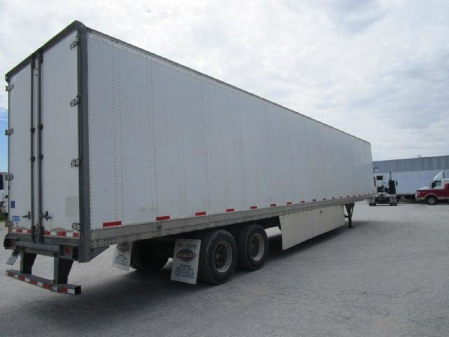 Trailer side view showing a 2012 Stoughton van trailer with triple axles, silver corrugated sides, rear doors, and reflective tape.