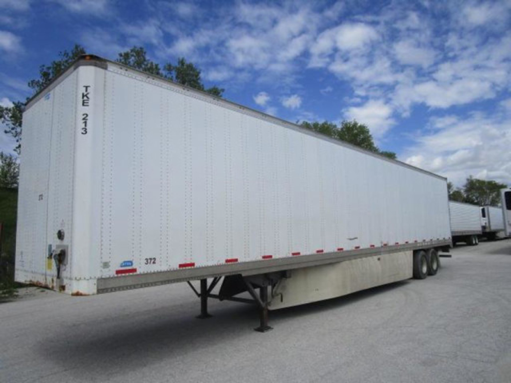 White Stoughton trailer with tandem wheels and landing gear, side view showing model 2012, empty cargo area, blue sky.