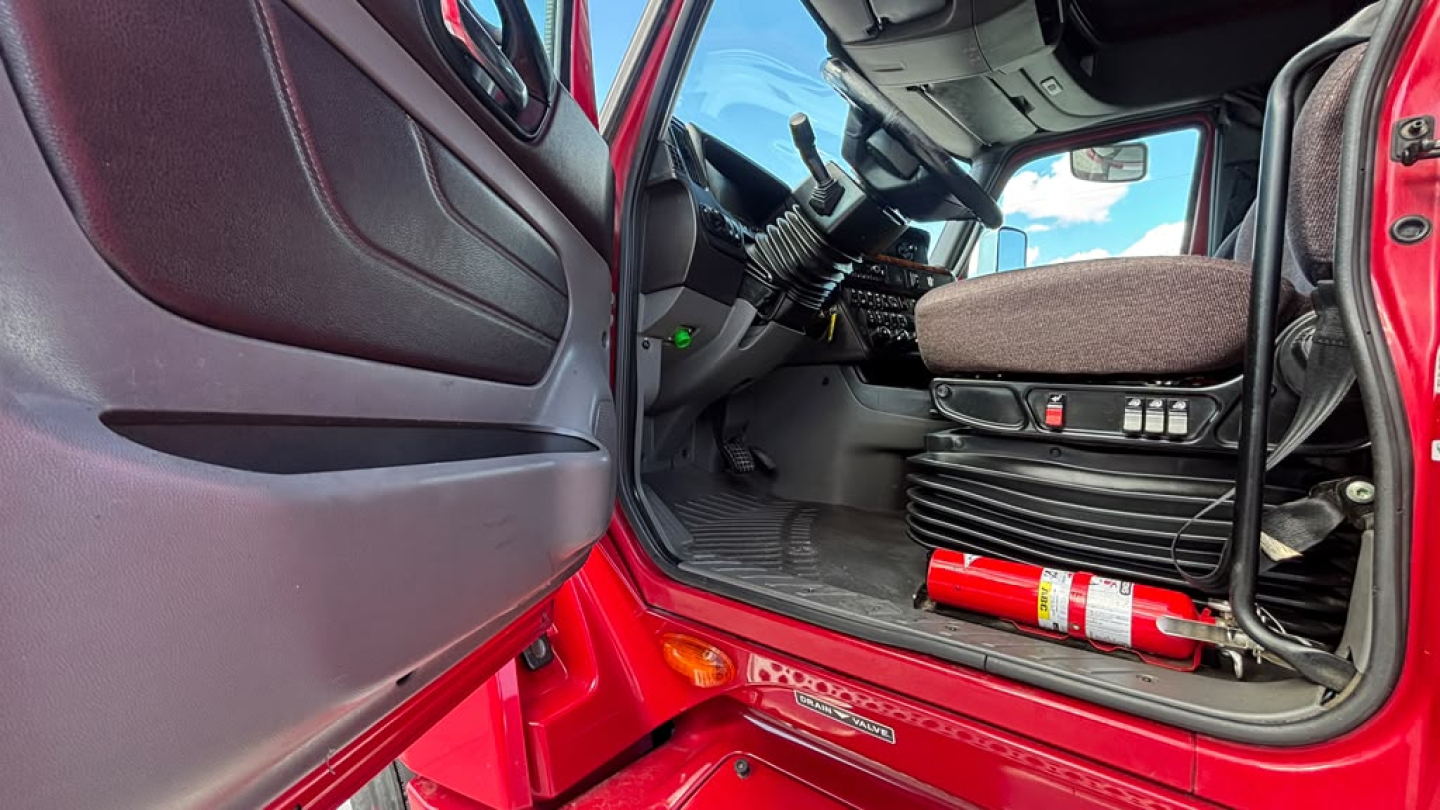 Cab interior of a 2022 International LT625 truck with red exterior, steering wheel, seat, and dashboard visible.