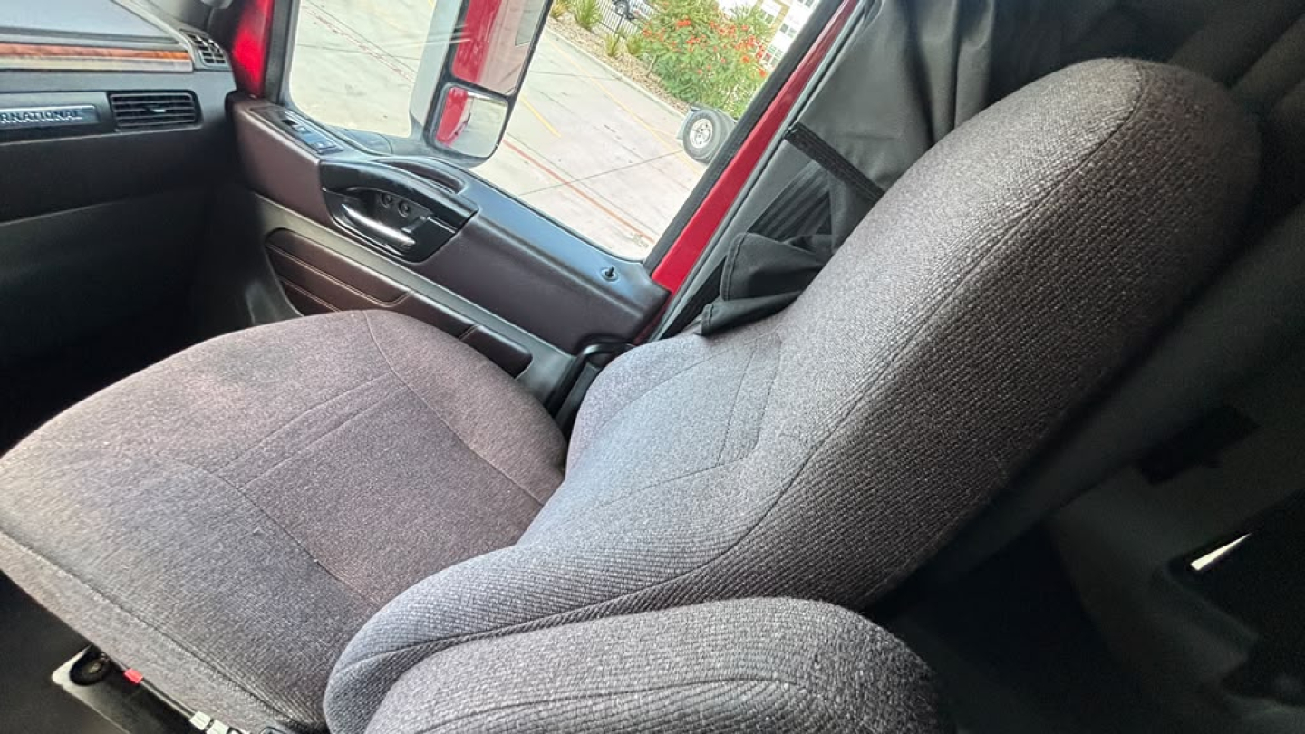 Truck cab interior showing grey fabric seats in a 2022 International LT625, front passenger and driver seats with door panel and window visible.