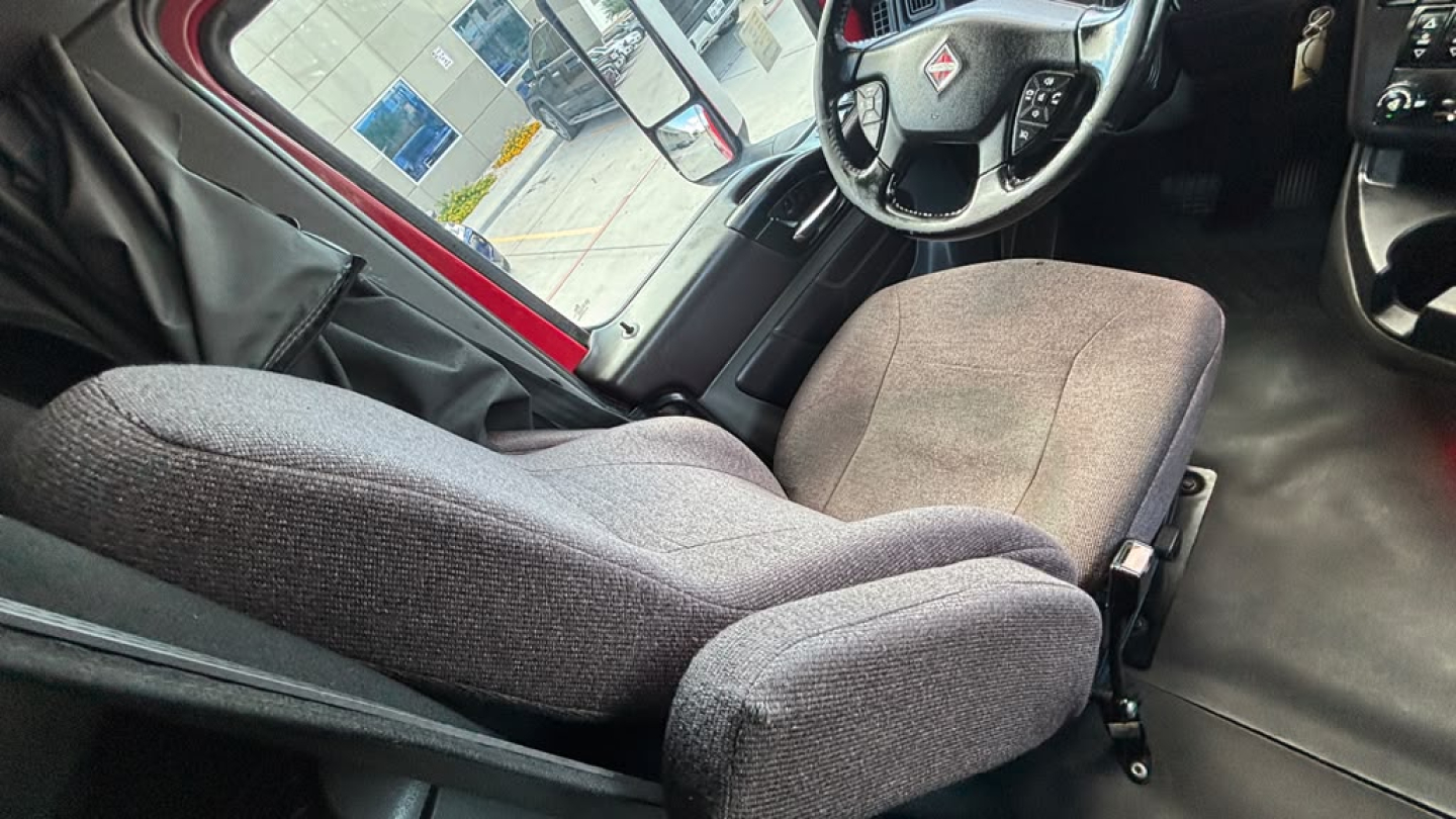 Truck cab interior showing driver seat and steering wheel; fabric seat upholstery; dashboard and center console visible.