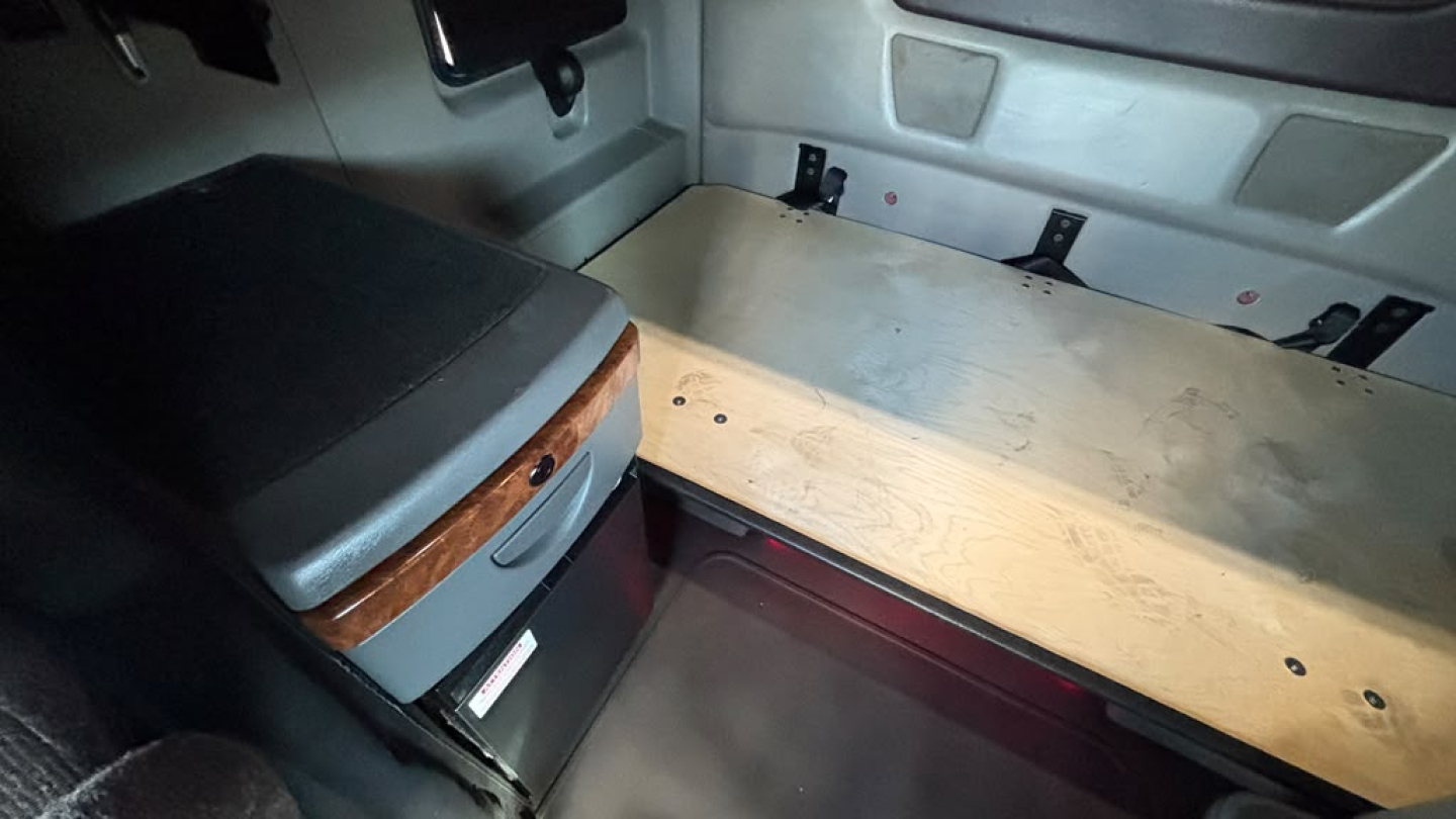 Truck cab sleeper interior with storage drawer and plywood bulkhead showing a flat sleeping area and side panels.