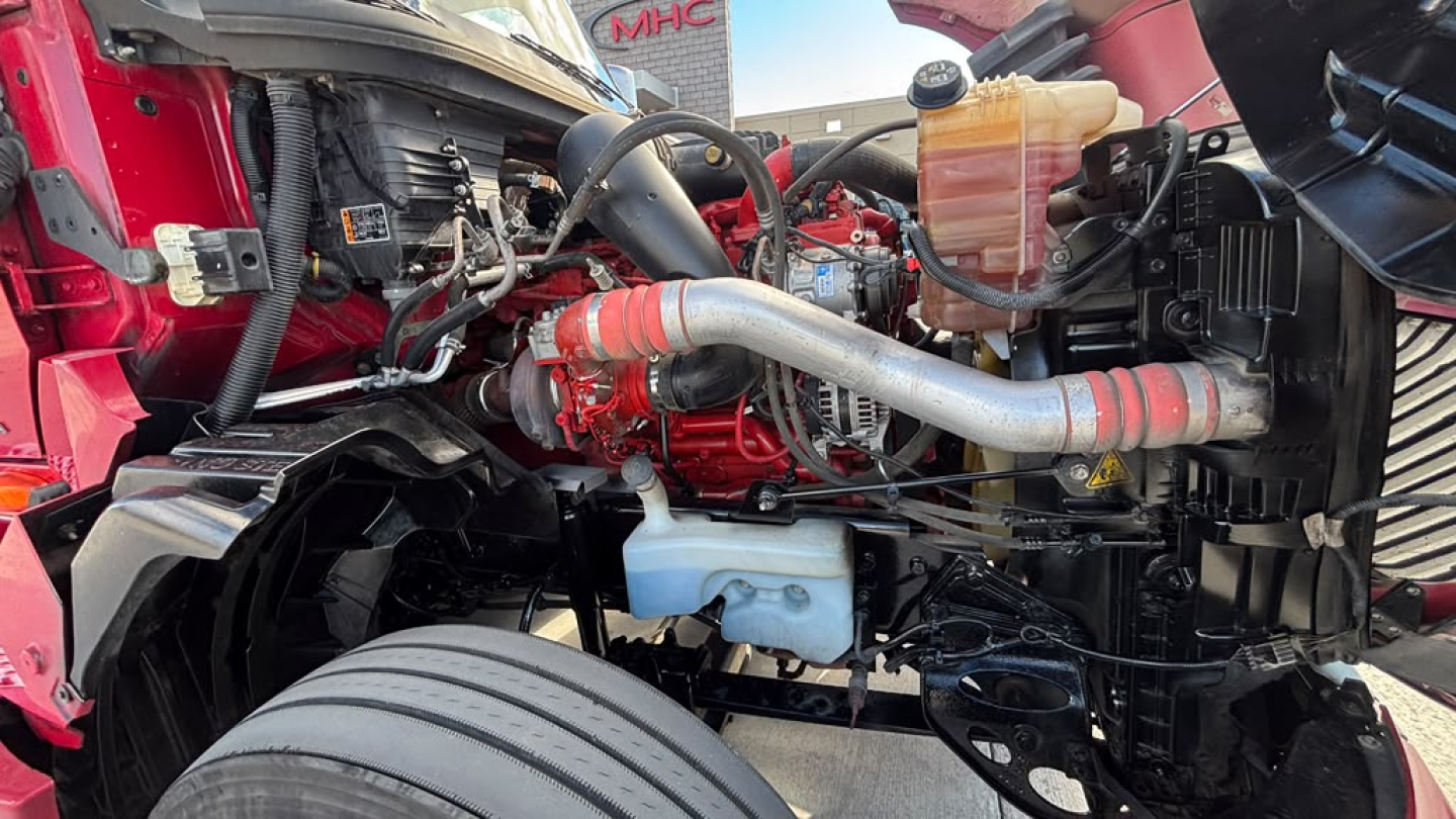 Truck engine bay with red exterior showing intake pipe, coolant reservoir, and various hoses in view; label details not legible.