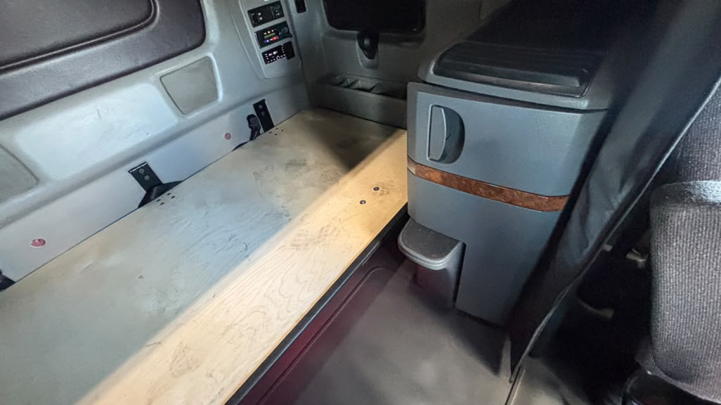 Interior of a 2022 International LT625 sleeper cab showing living area with light wood platform and center console with wood trim.