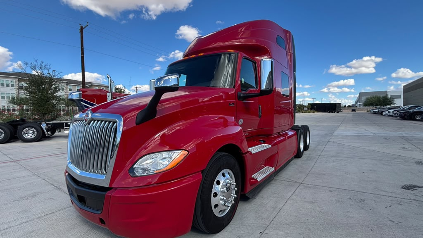 Red 2022 International LT625 tractor-trailer cab seen from front-left angle, glossy paint, chrome grille, large headlights, sleeper cab, parked in lot.