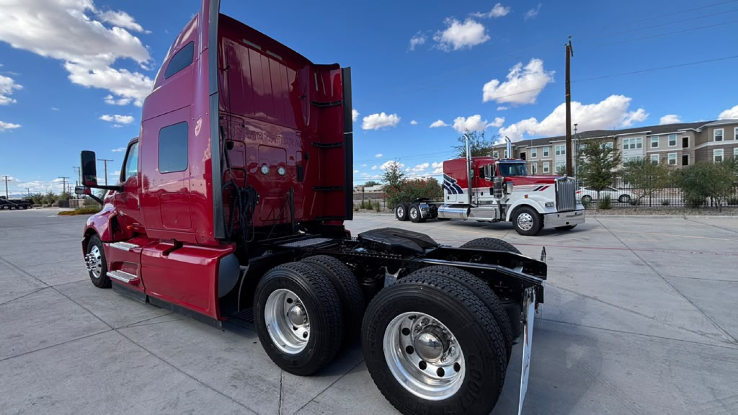 Red 2022 International LT625 semi-truck tractor with sleeper cab, left-rear view showing dual rear axles and sixth wheel, chrome fuel tanks, clear sky.