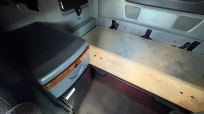 Truck cab sleeper interior with storage drawer and plywood bulkhead showing a flat sleeping area and side panels.