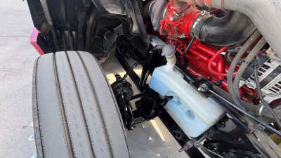 Truck engine bay showing radiator coolant reservoir, hoses, and a red-painted engine block with various components visible.