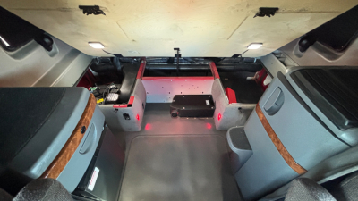Interior view of a sleeper cab indicating storage compartments and a central floor area, with red LED lights along the rear edge.