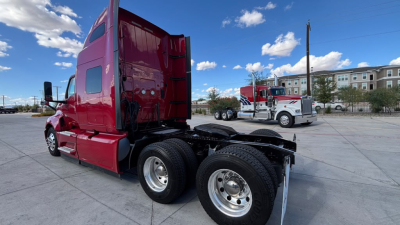 Red 2022 International LT625 semi-truck tractor with sleeper cab, left-rear view showing dual rear axles and sixth wheel, chrome fuel tanks, clear sky.