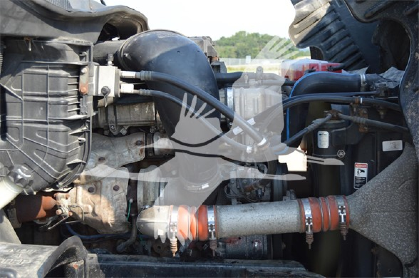 Conventional sleeper truck engine bay view showing exhaust piping, hoses, and coolant reservoir.