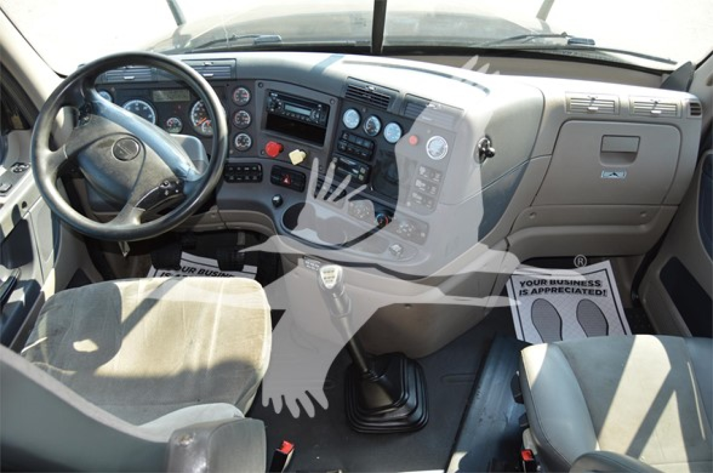 Freightliner Cascadia truck cabin interior showing steering wheel, dashboard with gauges, gear shift, and control panels.