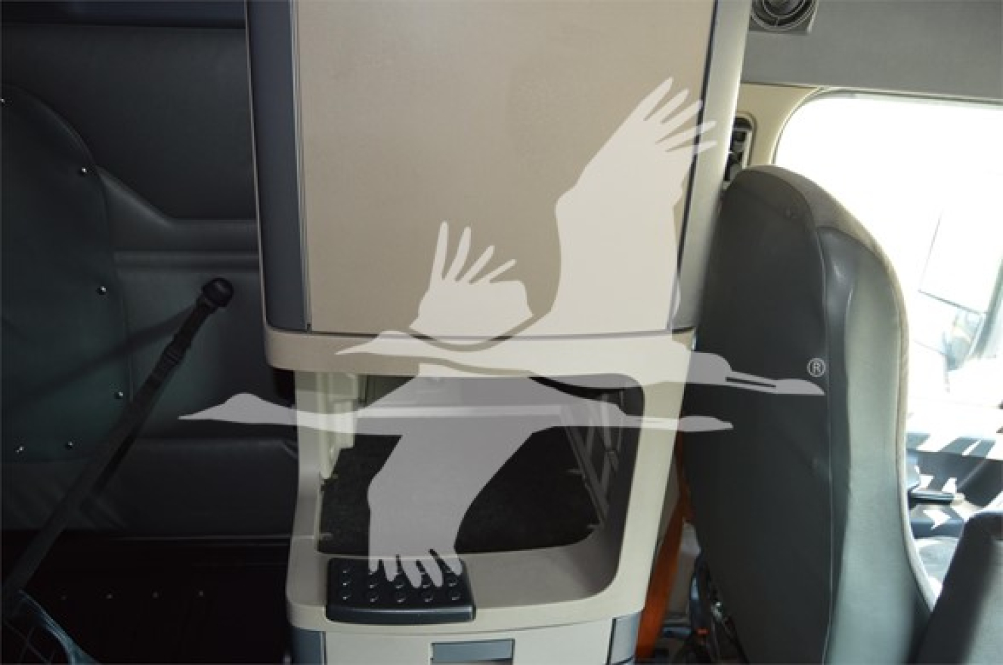 Cabin interior of a Freightliner Cascadia II Evolution sleeper, center console with small steps and storage; partial steering wheel visible; overhead cabinet closed.