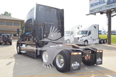 Truck rear view showing fifth wheel and dual rear axles, Freightliner badging not visible, reflective surface, parking lot with other trucks.