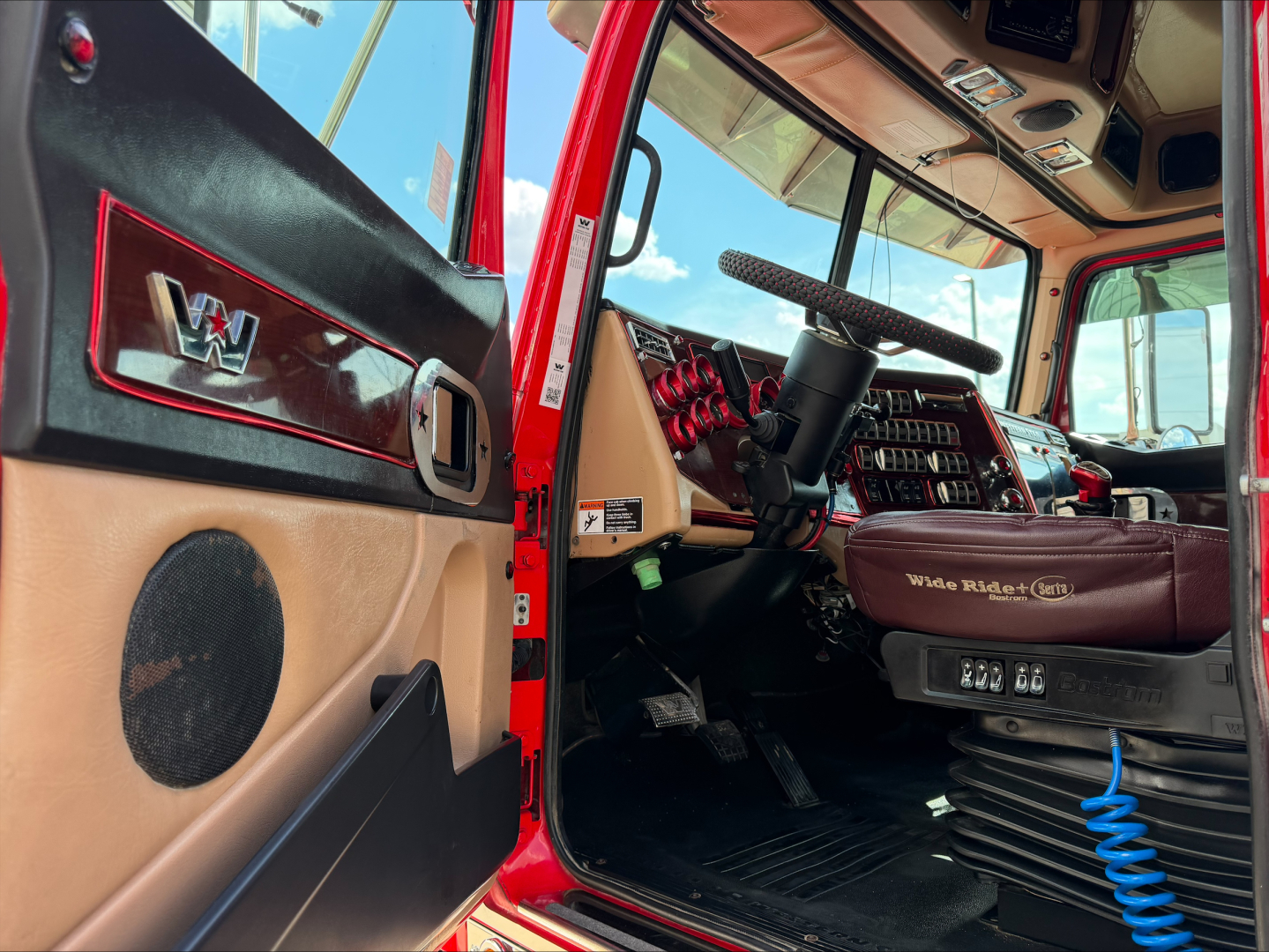 Western Star 4900 truck cab interior showing steering wheel, dash, and beige door panel with speaker.