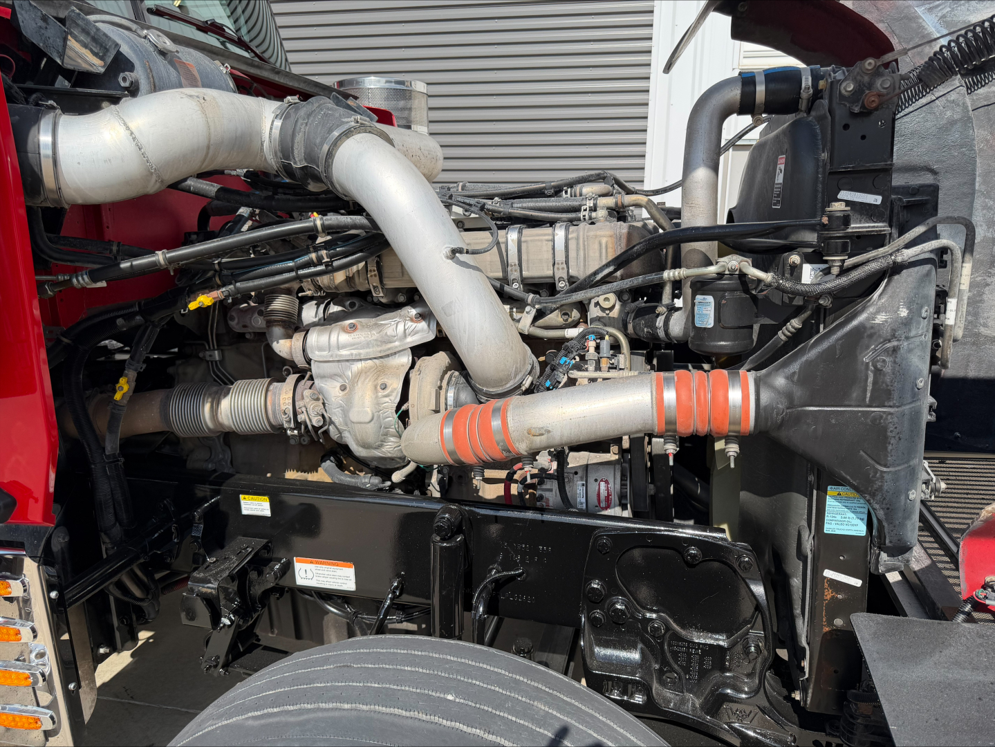 Truck engine bay of a 2020 Western Star 4900 showing large intake manifold, turbocharger, hoses, coolant reservoir, and radiator behind the front bumper.