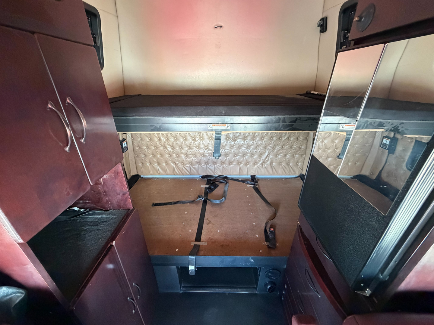 Interior of a Western Star 4900 sleeper cab showing back wall with diamond-plate bunk area, storage cabinets on left, mirrored panel on right, and bed straps.