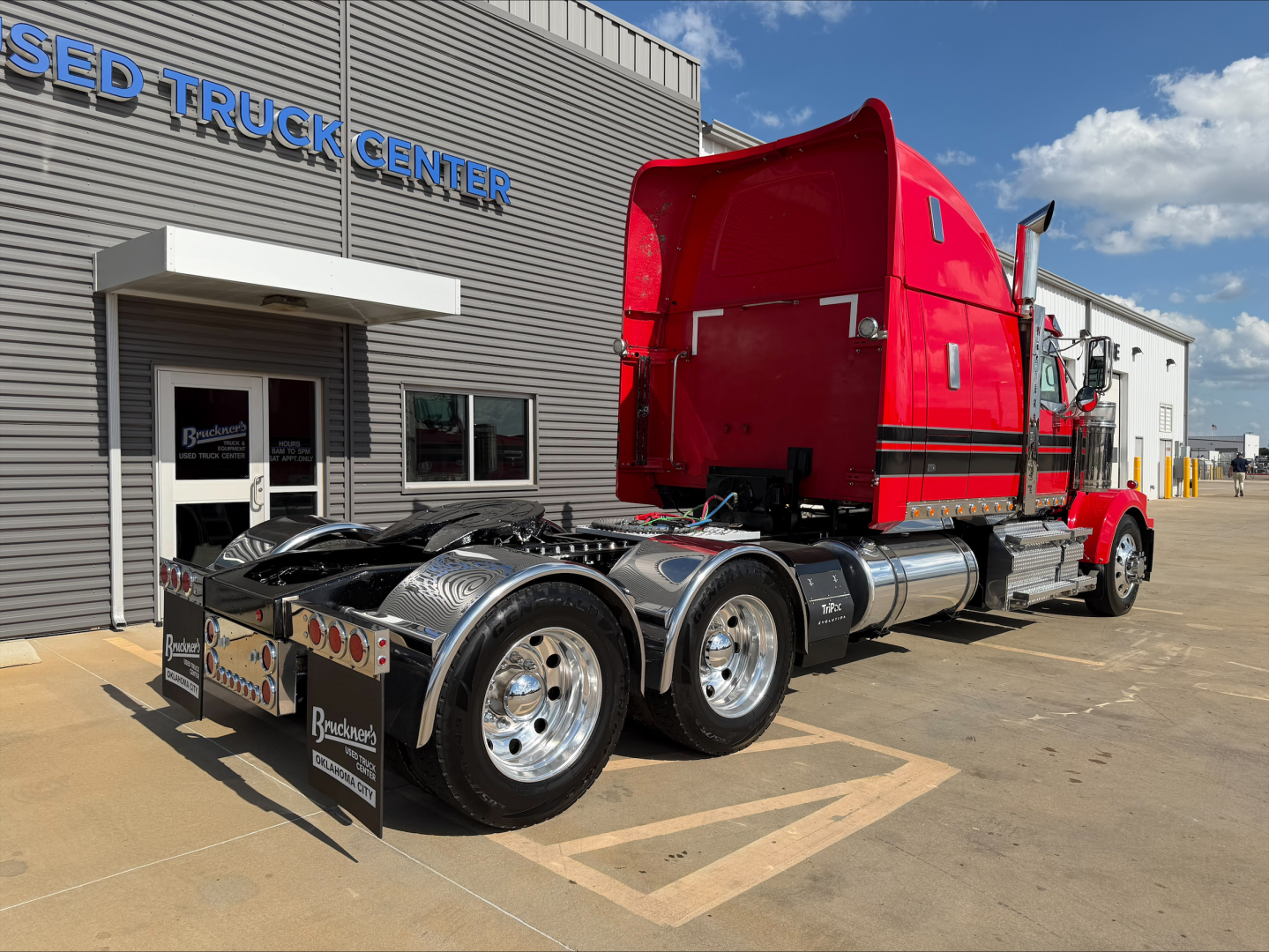 Western Star 4900 tractor in red with sleeper cab, showing rear tractor wheels and fifth wheel, parked outside used truck center.