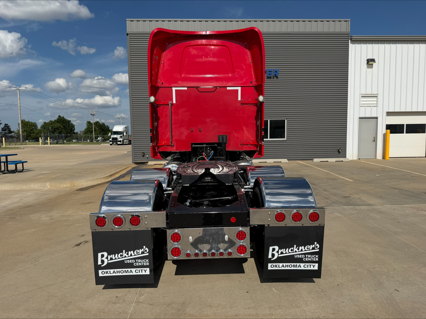 Rear view of a 2020 Western Star 4900 tractor with red sleeper cab roof and chrome fenders. Dual rear mud flaps show Bruckner’s Used Trucks Oklahoma City. Tail lights and fifth wheel area visible.