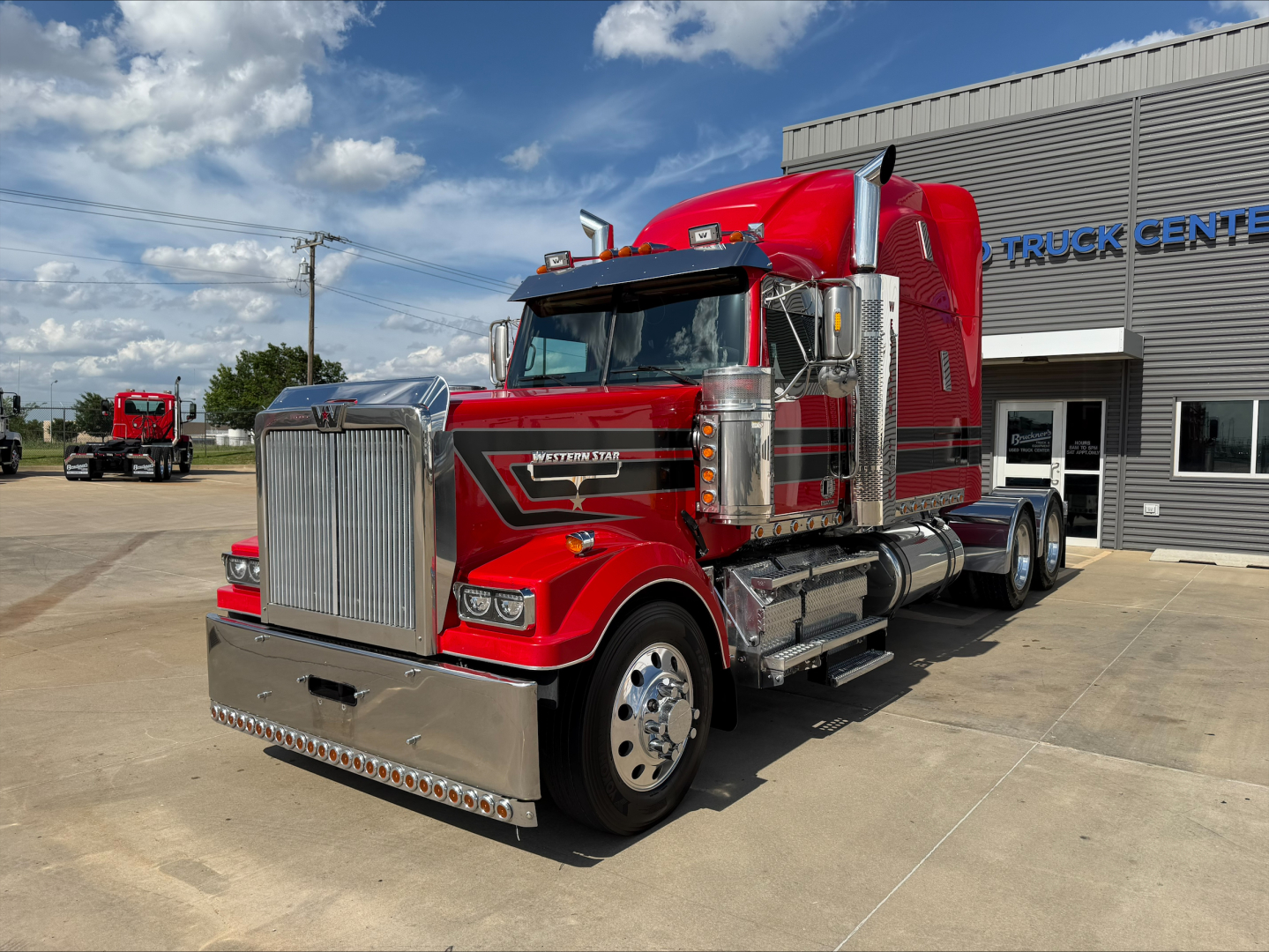 2020 Western Star 4900 truck in red with chrome accents and large grille, side exhaust stacks, parked outside a truck center.