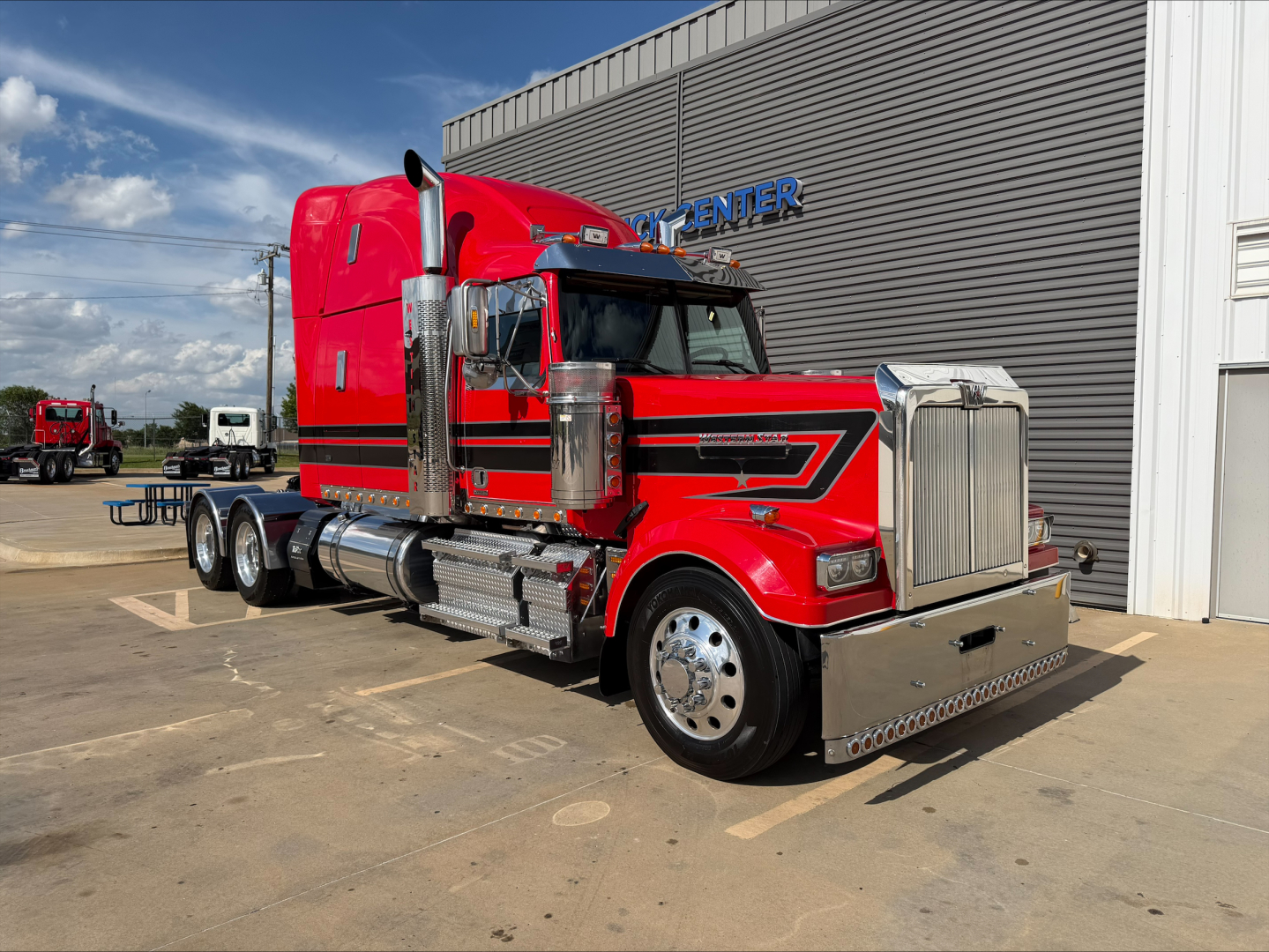 Western Star 4900Semi truck in red with chrome accents and dual rear axles, parked outside a building with blue sky.