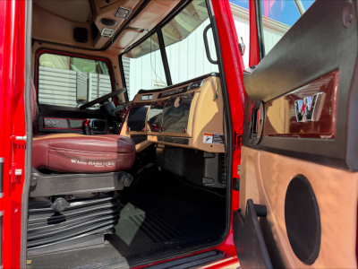 Western Star 4900 truck cab interior view with brown and tan dashboard, steering wheel, and driver seat; red exterior visible at door frame.