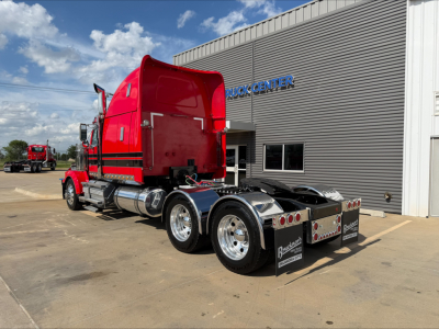 2020 Western Star 4900 conventional sleeper truck from rear-left side showing red cab, chrome fuel tanks, dual rear axles, and trailer hitch, dealership building in background.
