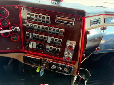 Truck cab dashboard with a red panel filled with numerous toggle switches and gauges, chrome accents, and control knobs visible.